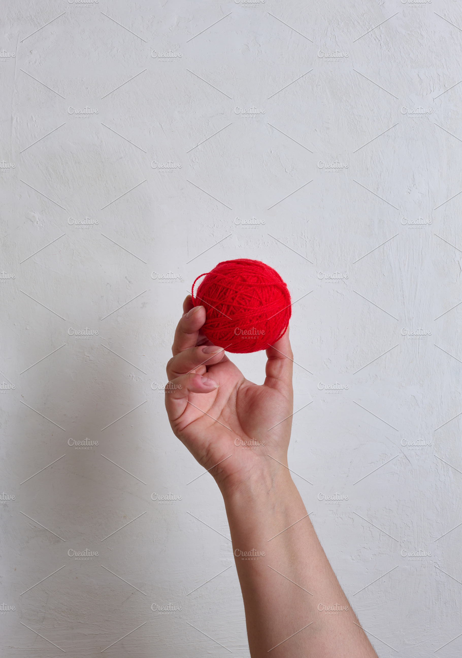 A person holding a red ball of wool yarn in their hand against a, a Person Photo by ndanko