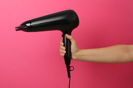 Female hand holds hair dryer on pink background, space for text, a Beauty & Fashion Photo by AtlasStudio PRO