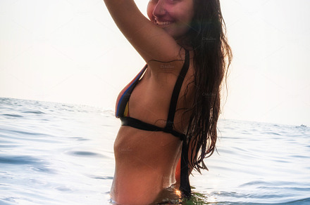 Young woman in bikini takes a bath in the sea at sunset lights i