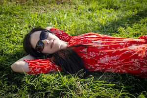 Woman in a red dress and sunglasses lying relaxed on a lush gree, a Person Photo by Imaginarium