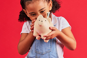 Little girl, excited and piggy bank savings in money planning, finance management or future investment on isolated red background. Smile, happy child and cash box in finance growth or budget learning, a Photo by Peopleimages.com
