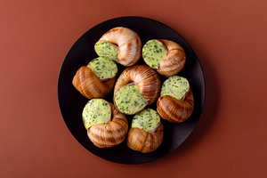 Top view of cooked escargot with garlic herb butter on a black p, a Food & Drink Photo by Ales Munt