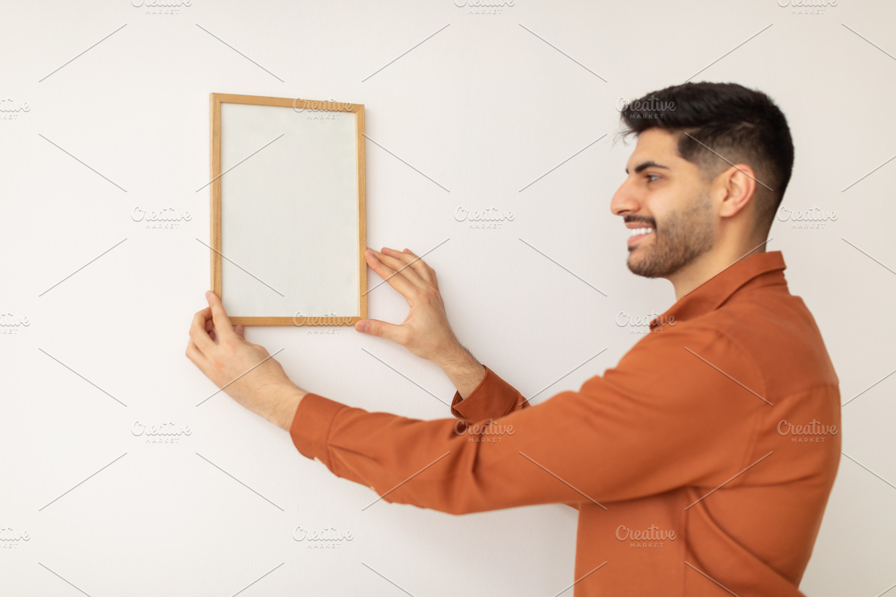 Portrait of cheerfcul man hanging photo frame on the wall, a Photo by Prostock-Studio