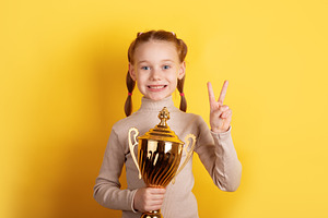 Smiling young girl with red hair holding a gold trophy and makin, a Person Photo by Ales Munt