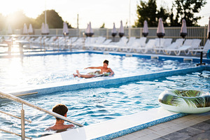 Children playing and relaxing in an outdoor swimming pool at sunset, a Photo by AS photostudio
