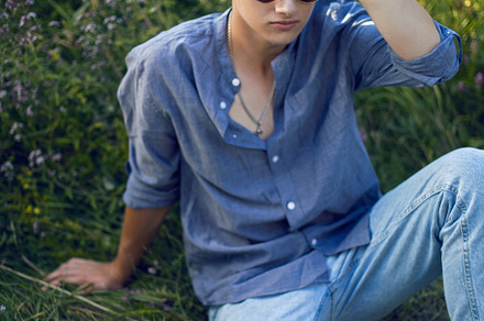 sexy teen guy in sunglasses is sitting on the grass in nature in a shirt and je, a Person Photo by SaulichPhoto