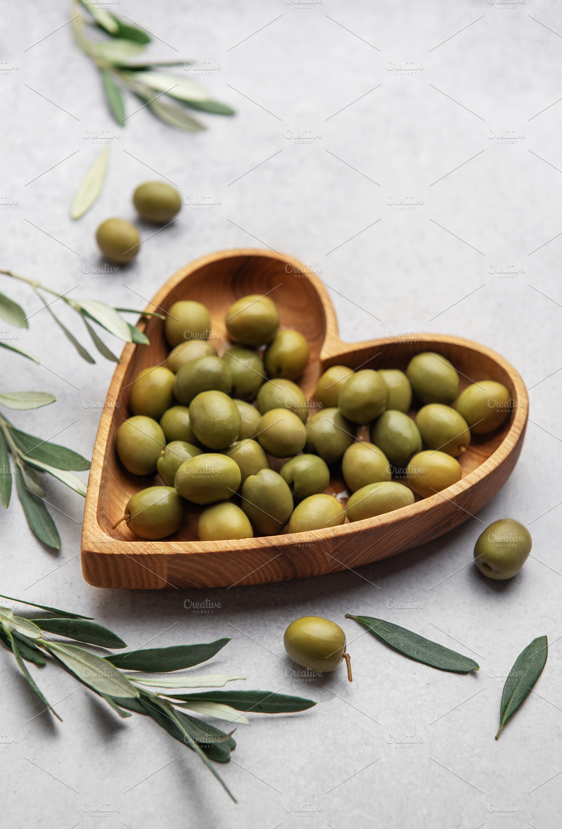 Fresh green olives displayed on wooden heart shaped bowl with ol, a Food & Drink Photo by Olena Rudo
