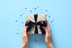 Female hands holding vintage gift box with blue ribbon bow on pastel blue backg