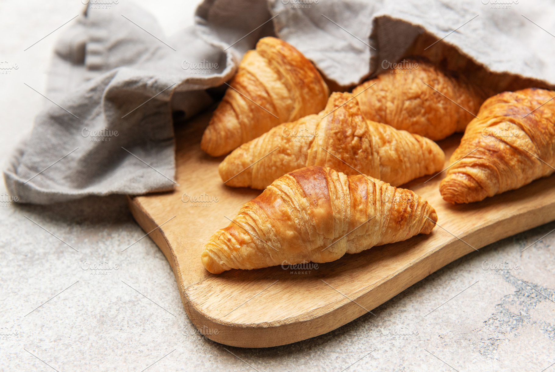Freshly baked croissants resting on wooden cutting board with li, a Food & Drink Photo by Olena Rudo