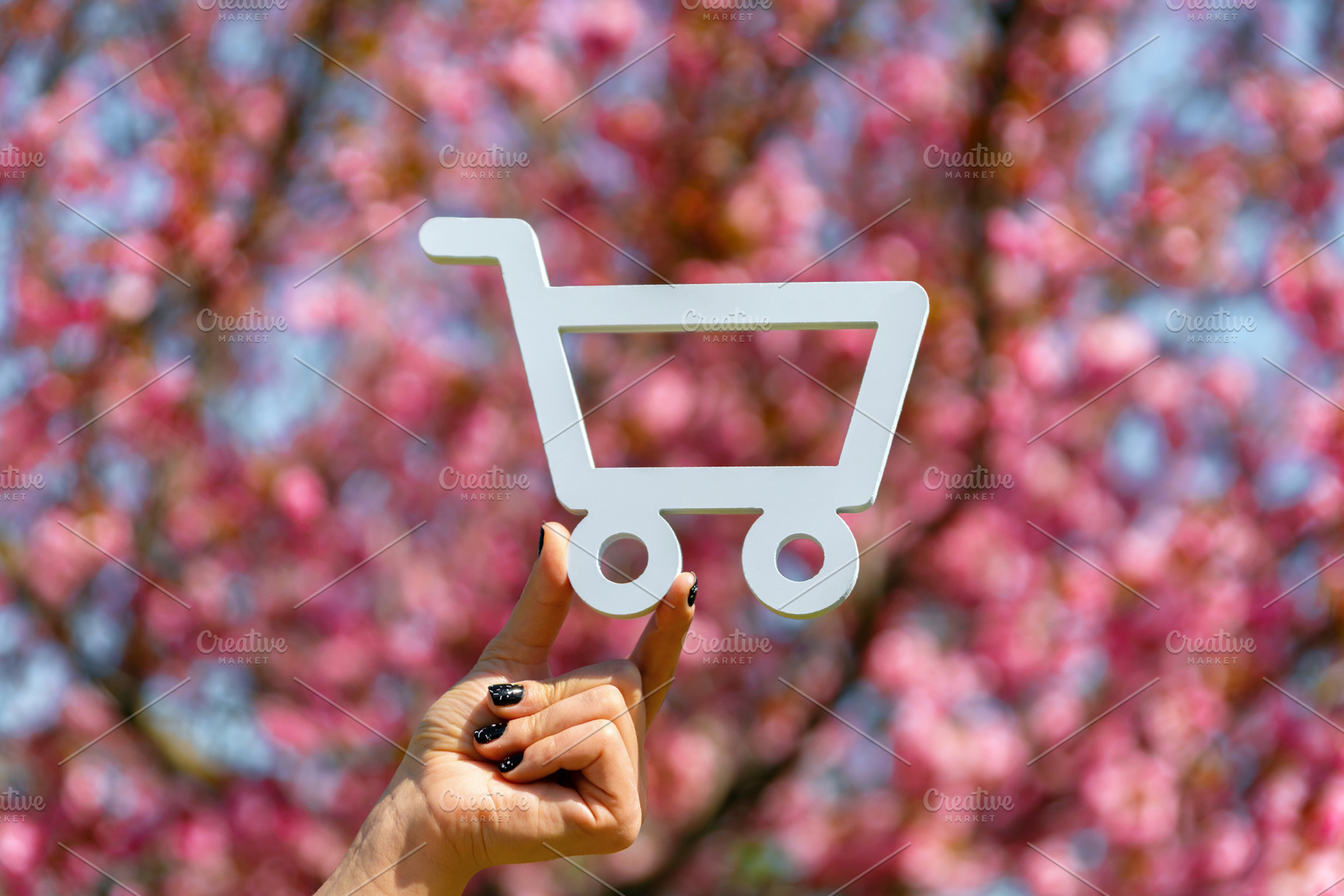 Hand holding a white shopping cart cutout with a backdrop of vib, a Nature Photo by Ales Munt
