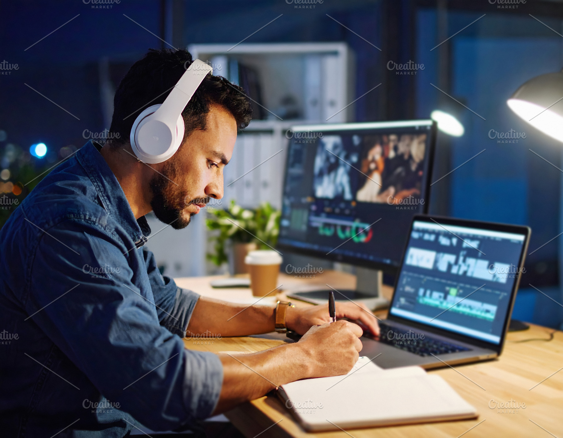 Businessman wearing headphones taking notes while editing on lap, a Business Photo by GoodGoods