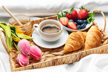 Romantic breakfast in bed with coffee, croissants, berries, hone