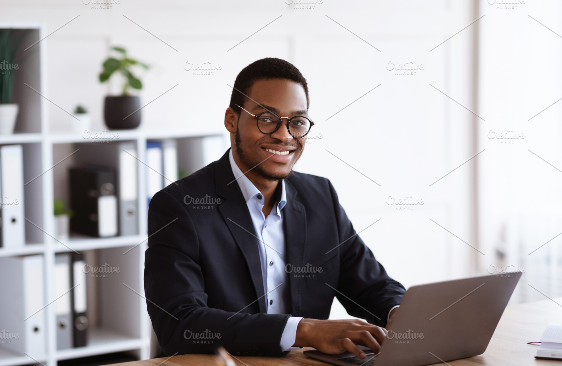 Cheerful african businessman working with laptop in office, a Photo by Prostock-Studio