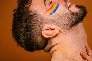 Bearded man expressing pride with rainbow face paint, a Photo by karrastock