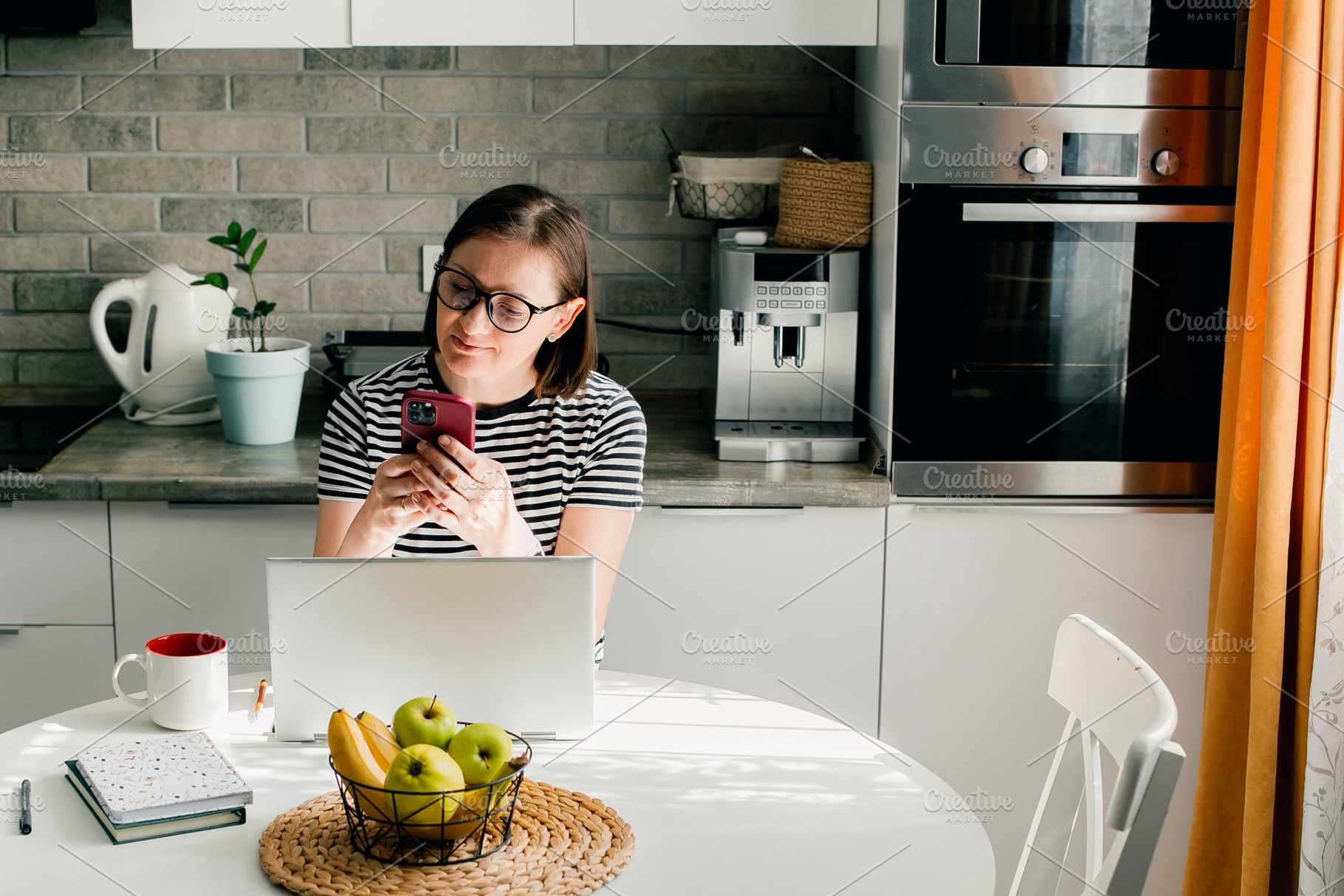 Freelancer woman wearing glasses using phone and laptop while working from home, a Person Photo by Anikona