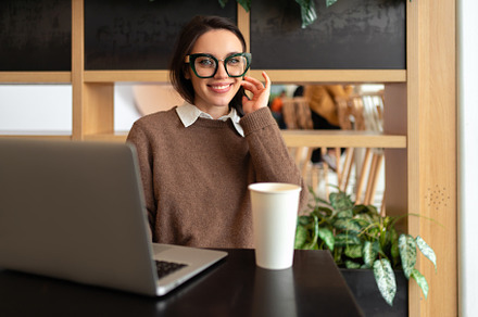 Young adult smiling woman with glasses sits at workstation, a Photo by andreonegin market