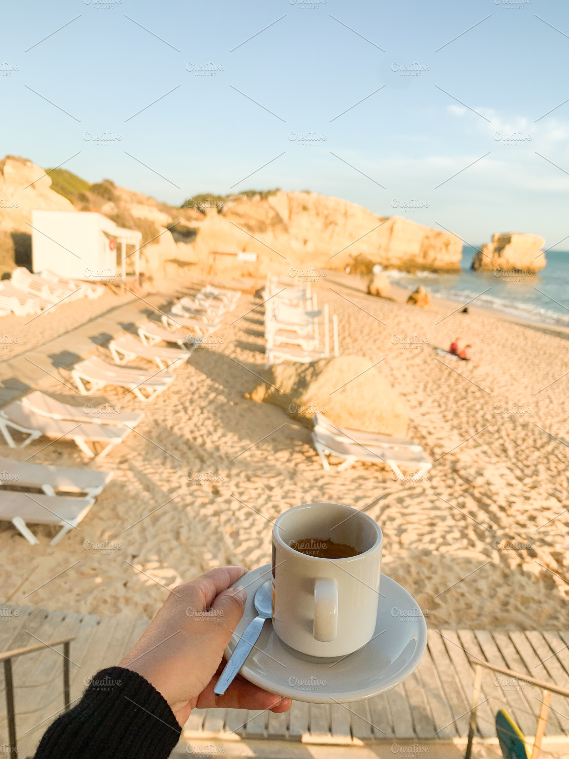 Hand holding coffee cup against the backdrop of a golden sandy b, a Holiday Photo by sebastianaraw