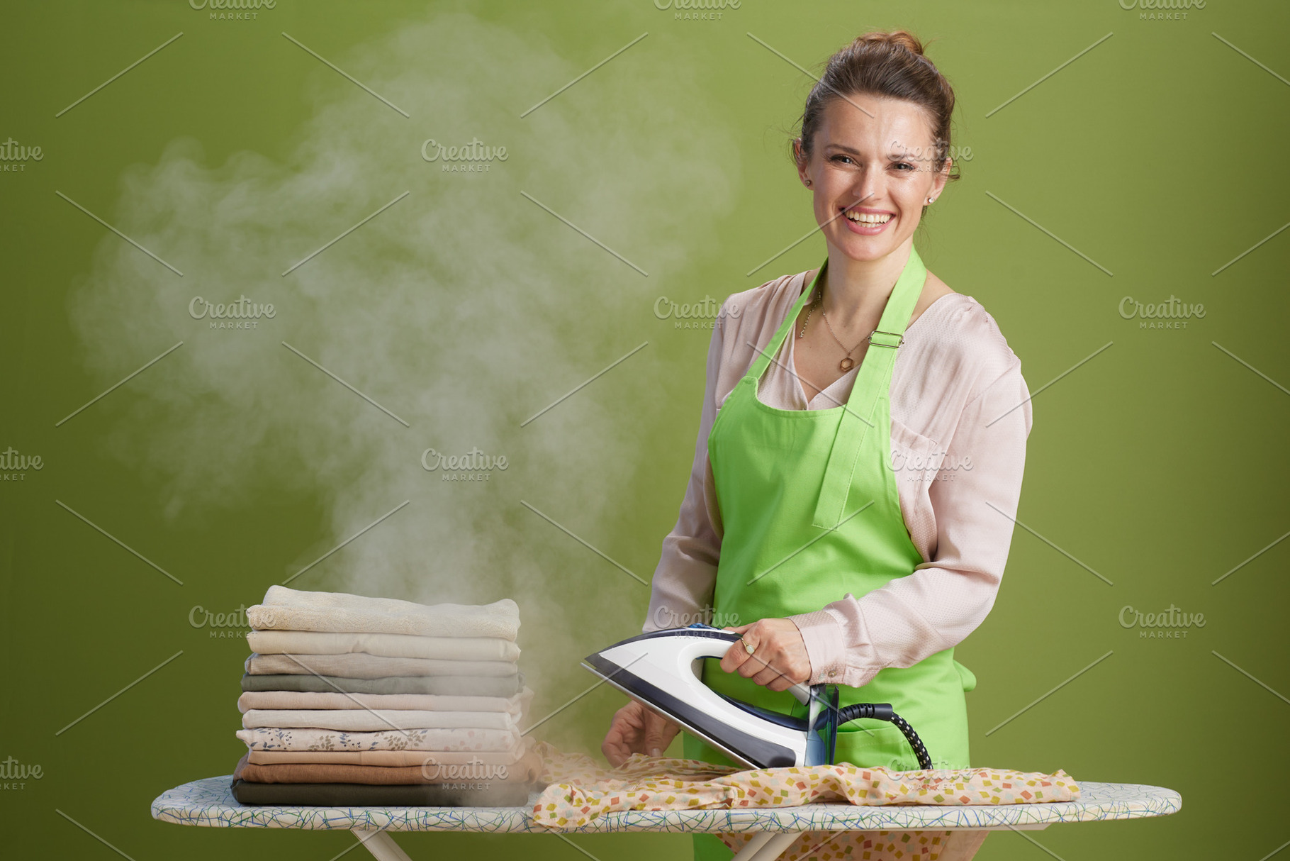 Smiling woman ironing stack of clothes with steam, a Person Photo by Alliance Images