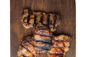 Three grilled steaks on a wooden board, isolated background, a Food & Drink Photo by ndanko