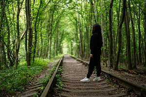 Woman walking along forest railway tracks surrounded by lush green trees, a Photo by AS photostudio