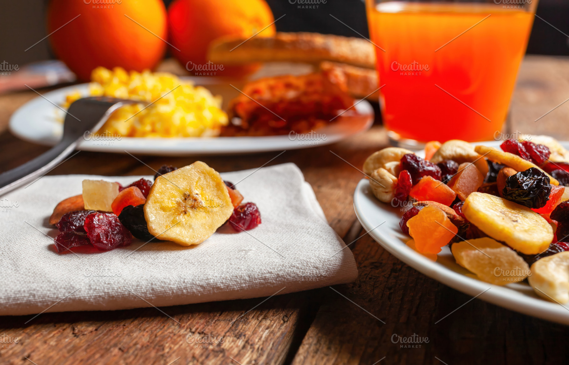 Dried fruit mix, orange juice and scrambled eggs composing a healthy breakfast, a Food & Drink Photo by Antonio Gravante Market