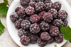 Frozen blackberries on white plate with fresh leaves, a Food & Drink Photo by Olena Rudo