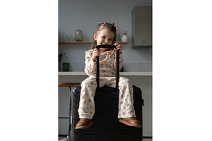 Little girl sitting on a suitcase in, a Holiday Photo by undrey