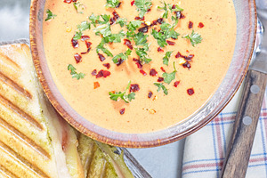 Red bell pepper cream soup served with grilled turkey panini, vertical top view