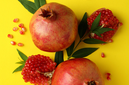 Ripe pomegranate, leaves and seeds on yellow background, a Food & Drink Photo by AtlasStudio PRO