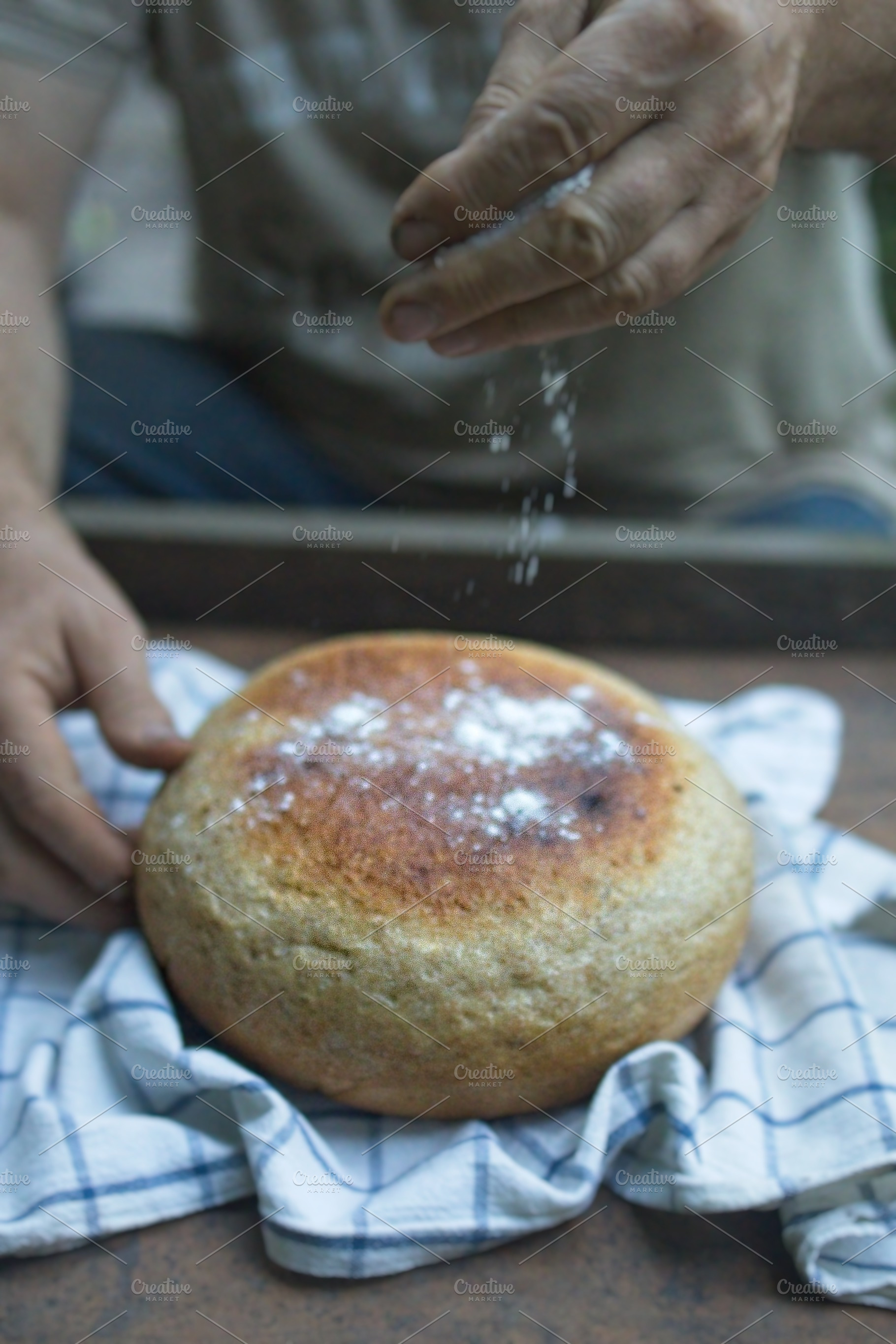 Baker's hand sprinkles flour on fresh bread close-up. A man finishes baking, de, a Food & Drink Photo by TanaCh