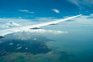 Airplane wing above coastline and clouds in bright sky, a Transportation Photo by GoodGoods
