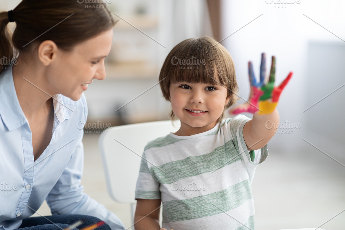 Happy little boy showing painted colorful hand and smiling to camera, sitting a, a Photo by Prostock-Studio (Photo 1 of 2)