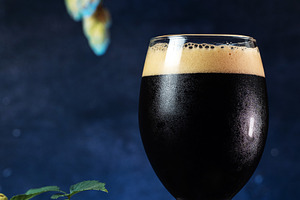 Glass of beer stout on a dark blue background, green hops, a Food & Drink Photo by PavelKant