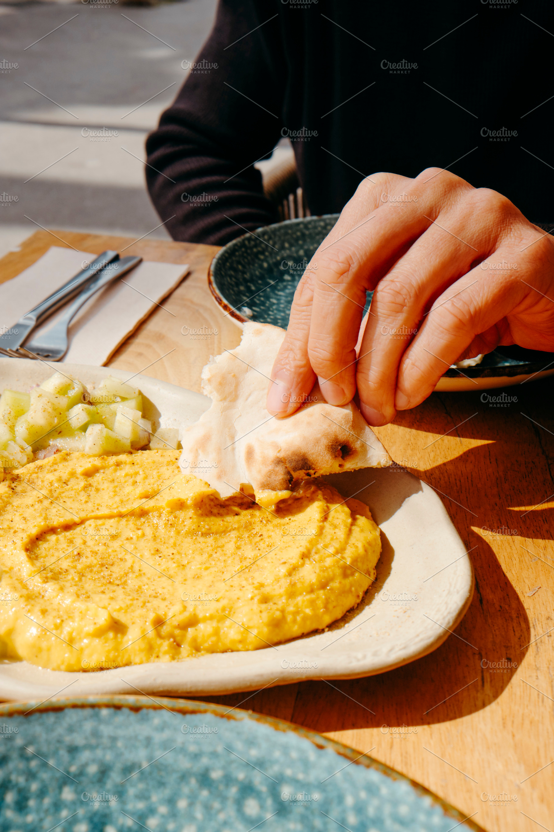 man dips a piece of naan bread on hummus, a Photo by Nito