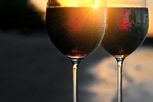Romantic beach scene: two glasses of red wine at sunset near water
