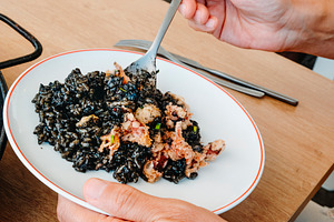 at a restaurant, a man serves himself arros negre, a Photo by Nito