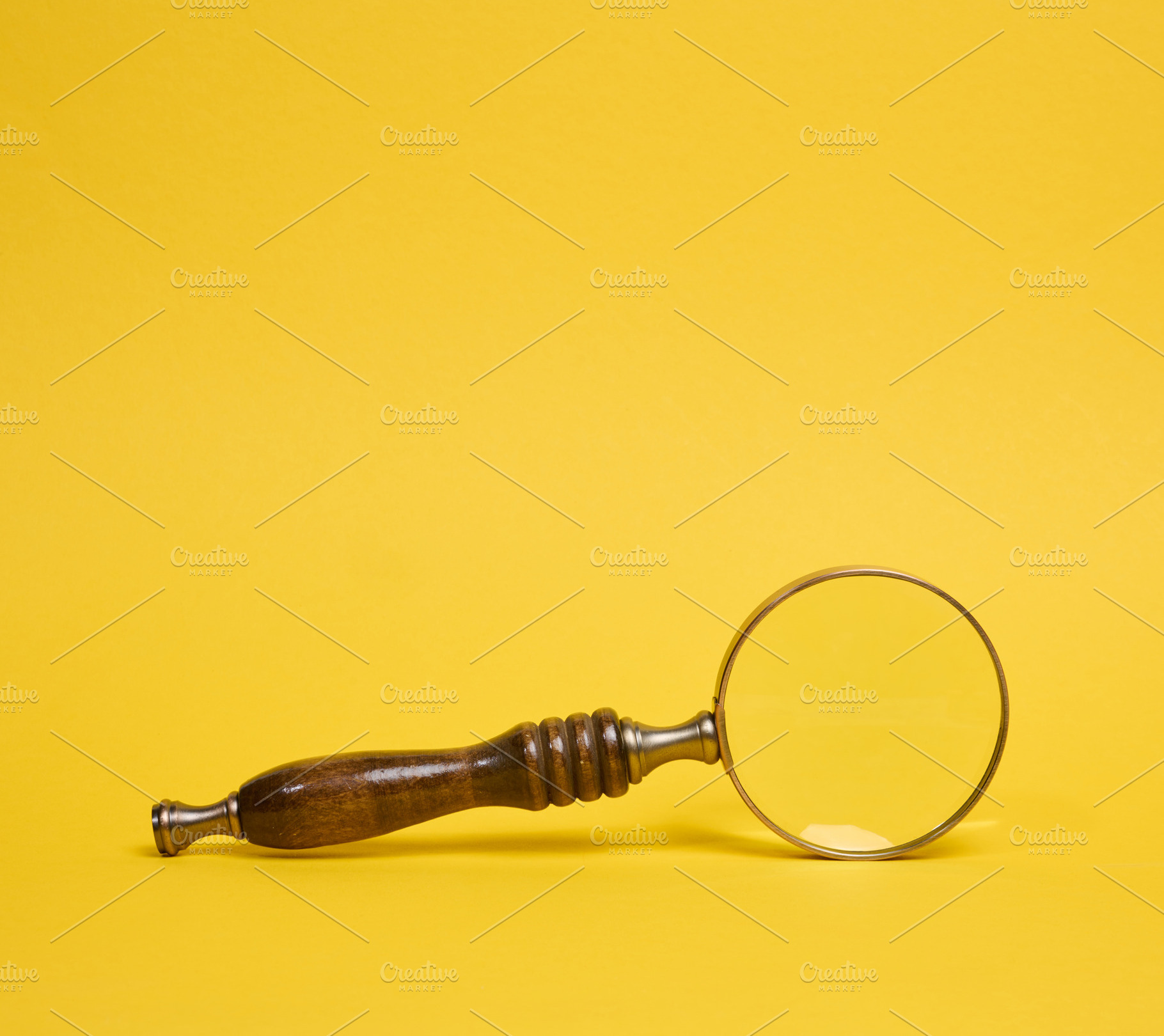 A vintage magnifying glass with a wooden handle lying on a yello, a Business Photo by ndanko