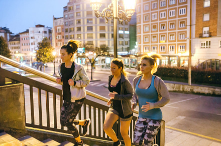 Women friends training running up stairs in city at night
