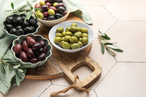 Green, black and kalamata olives in bowls on wooden board, a Food & Drink Photo by Olena Rudo