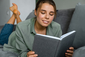 Pleased beautiful woman reading book while lying on sofa
