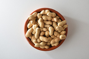 Heap of peanuts with skin in clay bowl on table, a Food & Drink Photo by Davizro's Market