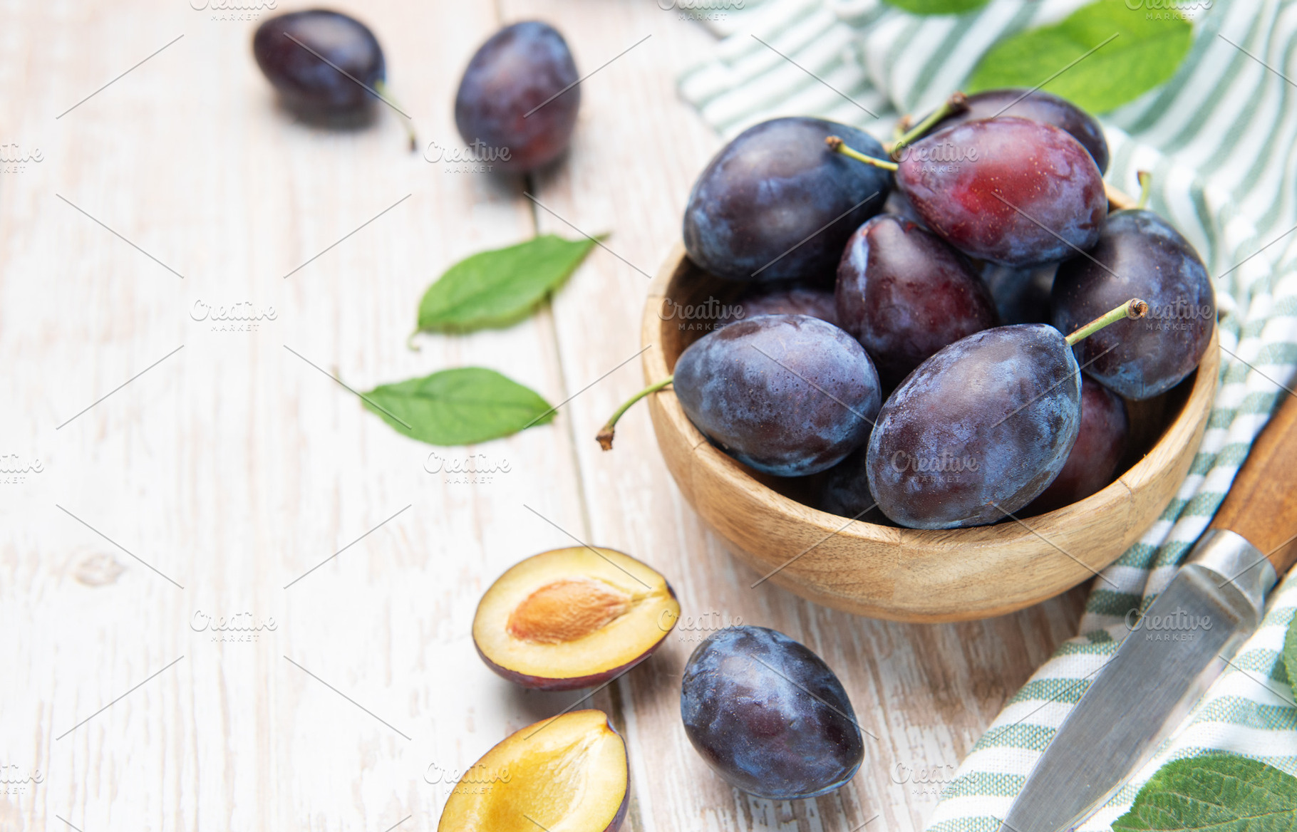 Fresh plums in wooden bowl with knife, a Food & Drink Photo by Olena Rudo