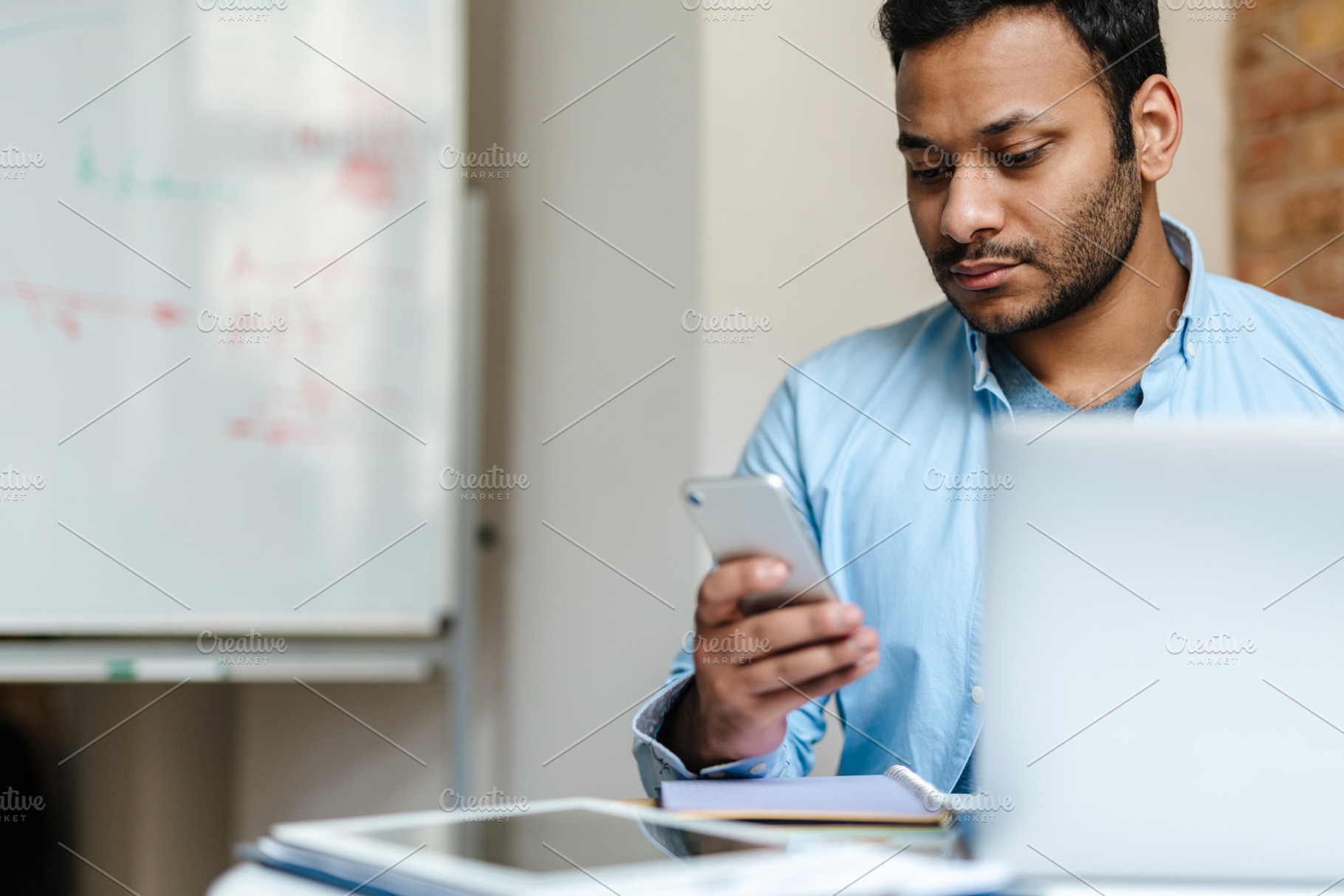 Middle eastern unshaven man using mobile phone while working with laptop, a Person Photo by Dean Drobot
