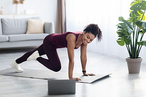 Sporty african american woman exercising at home, looking at laptop