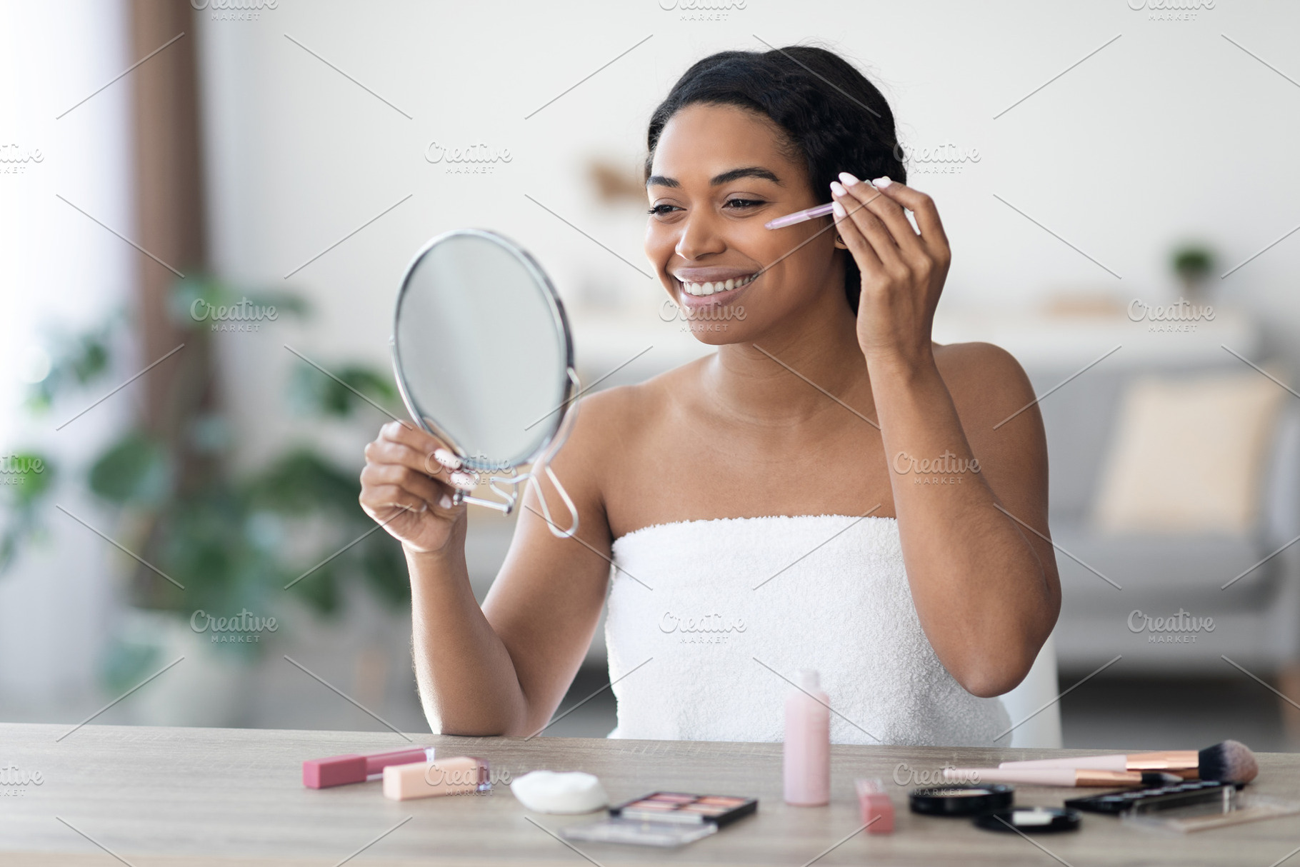 Attractive black woman applying concealer after shower, a Photo by Prostock-Studio