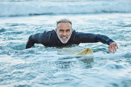 Senior man, water and sports surfer on a beach with smile training for fitness and health or hobby in the outdoors. Elderly male paddling on surfboard for healthy exercise in the ocean waves at sea, a Photo by Peopleimages.com