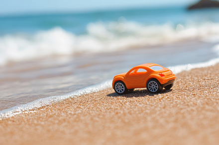Orange toy car rests on sandy beach, a Photo by Iftikhar Alam