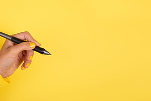 Female hand holding a black pen against a vibrant yellow backgro, a Business Photo by Ales Munt