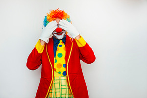 Clown covering eyes with both hands, a Person Photo by karrastock