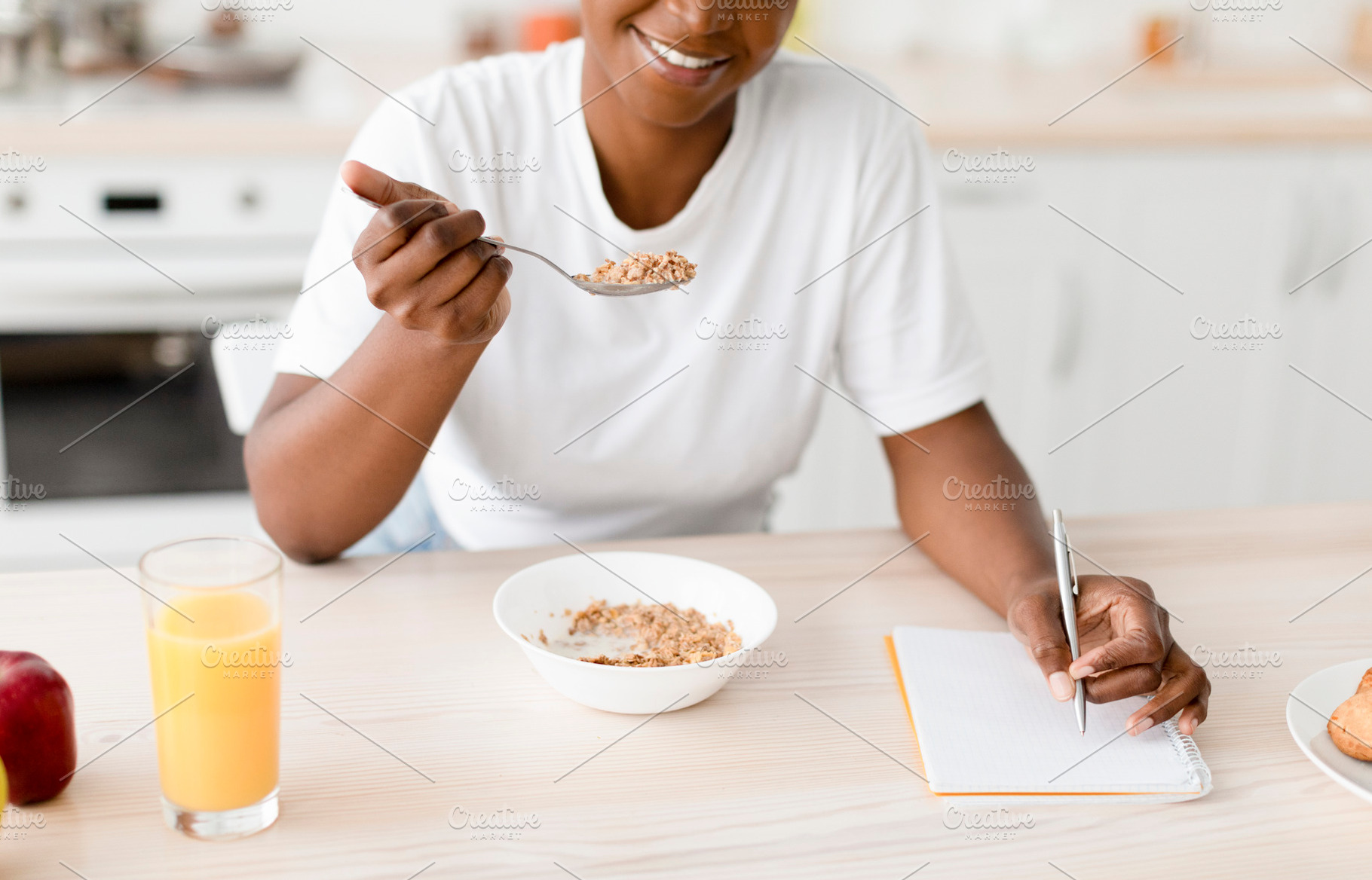 Smiling millennial black female eating porridge at table with cookies, juice an, a Person Photo by Prostock-Studio